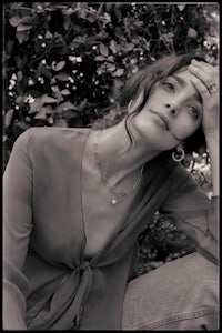 a black and white photo of a woman leaning against a tree